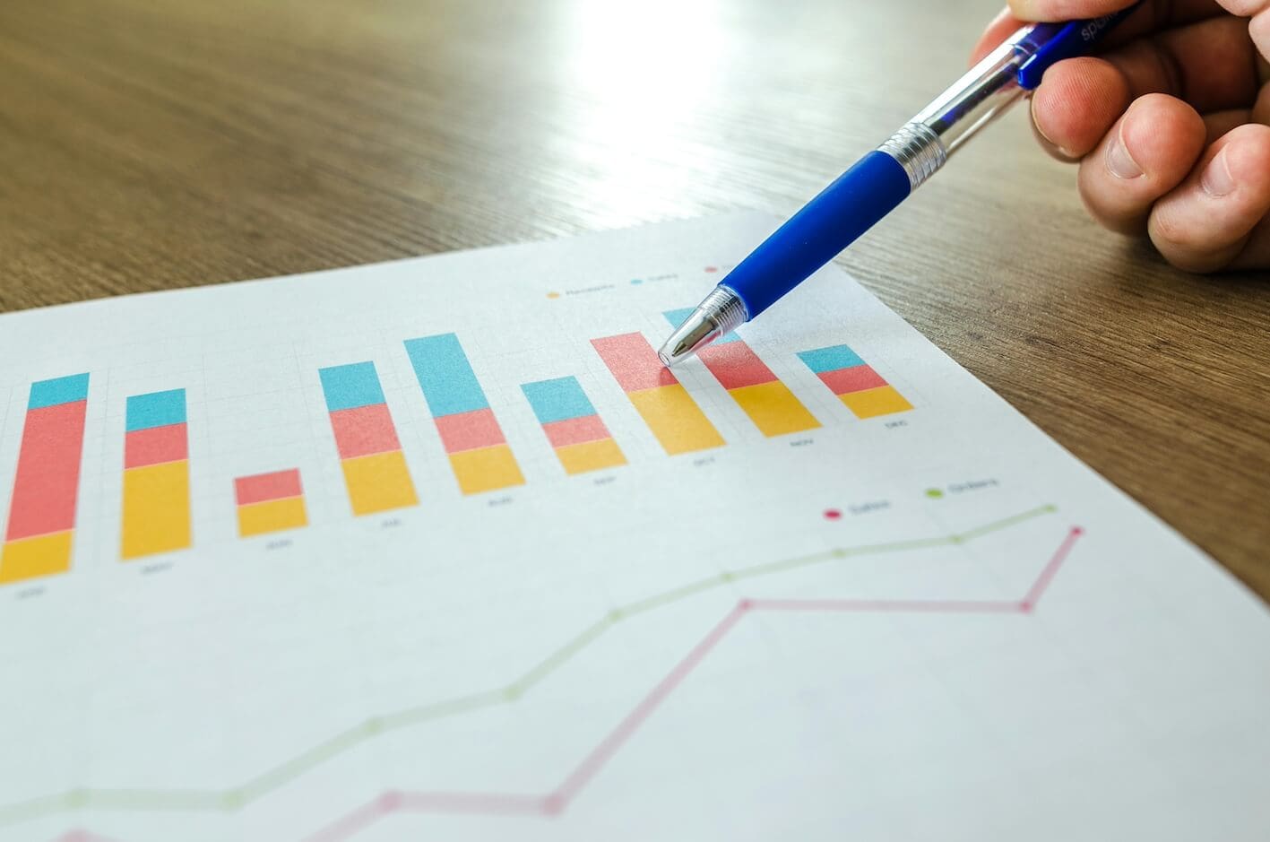 Eine Person hält einen Stift auf einem Papier mit Grafiken, die SEO und Schlüsselwörter zeigen.