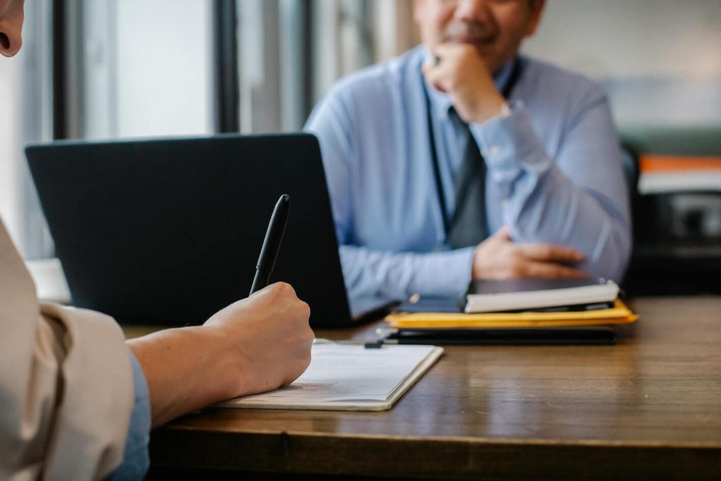 Eine Person hält einen Stift vor einem Mann, der an einem Tisch sitzt und Arbeitsgeberbewertungen bespricht.