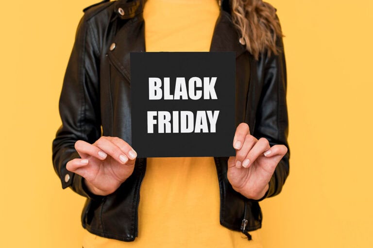 Eine Person in schwarzer Lederjacke und gelbem Hemd hält ein schwarzes Schild mit der Aufschrift "BLACK FRIDAY" in weißen Großbuchstaben auf gelbem Hintergrund - perfekt für Dienstleister, die neue Kunden anlocken wollen.